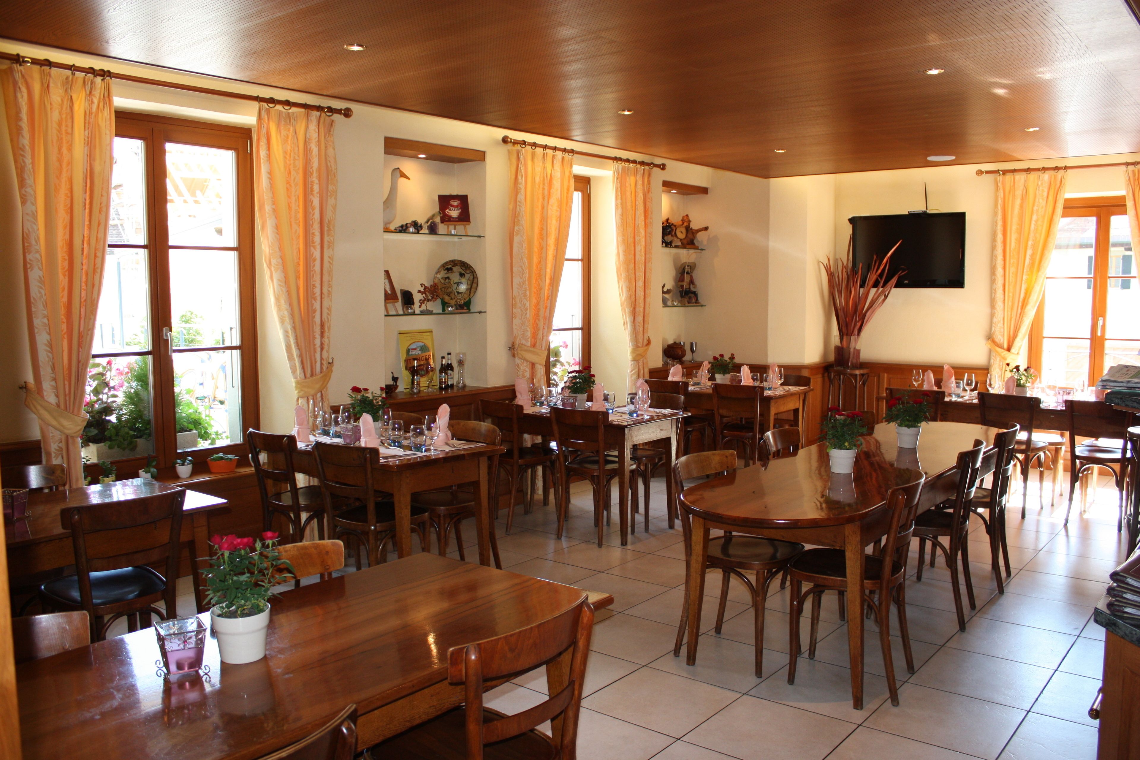 Un restaurant avec des tables et des chaises en bois, des plantes en pot et un téléviseur fixé au mur.