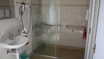 Une salle de bain avec une douche à parois de verre, un lavabo avec un porte-serviettes et une poubelle.