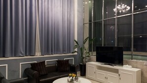 Un salon moderne doté d’une grande fenêtre, d’un téléviseur, d’un canapé, d’une table basse et d’un lustre.
