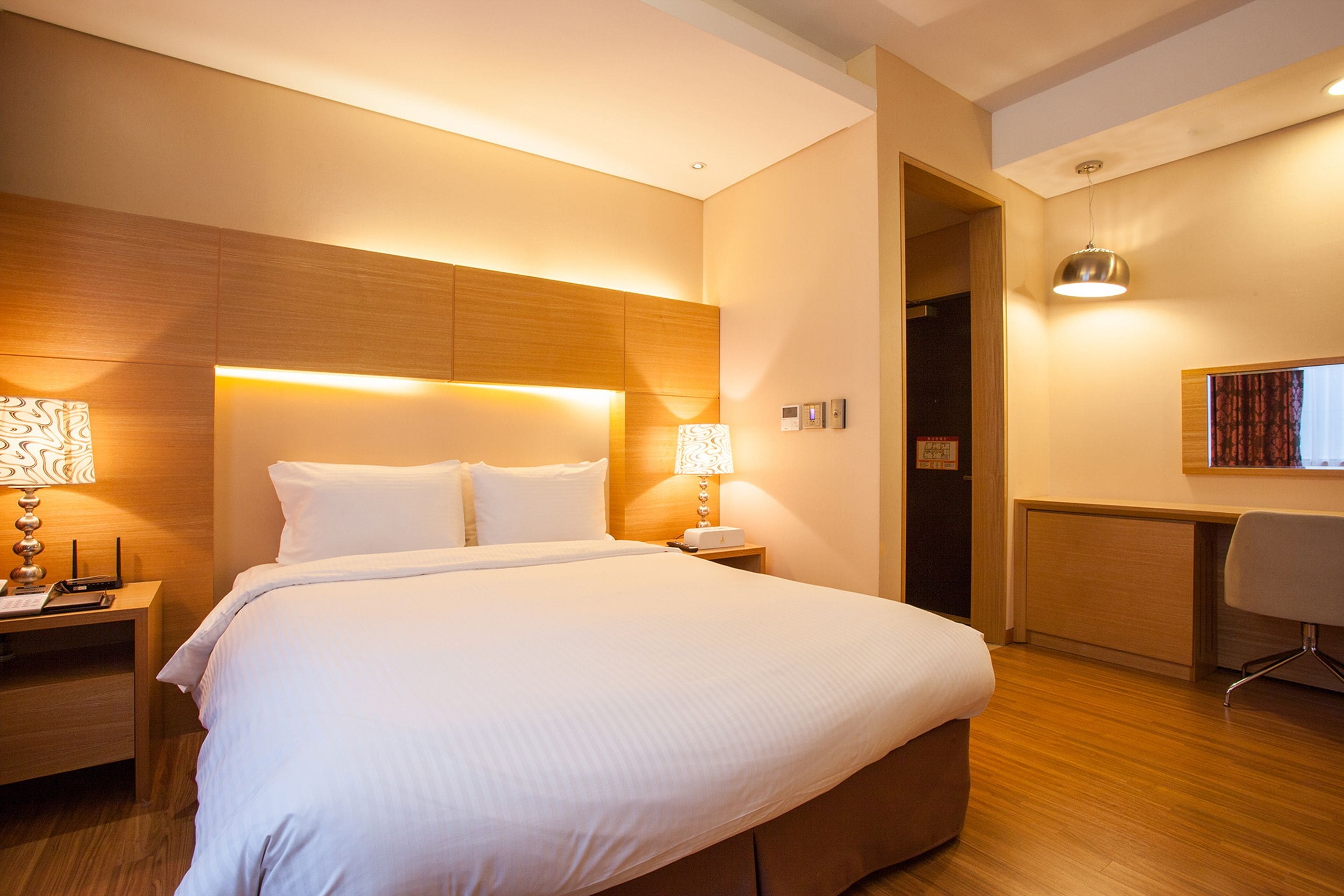 A hotel room with a large bed, bedside lamps, a desk, and a chair.
