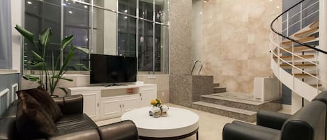 A modern living room with a television, leather sofa, white coffee table, and a spiral staircase.