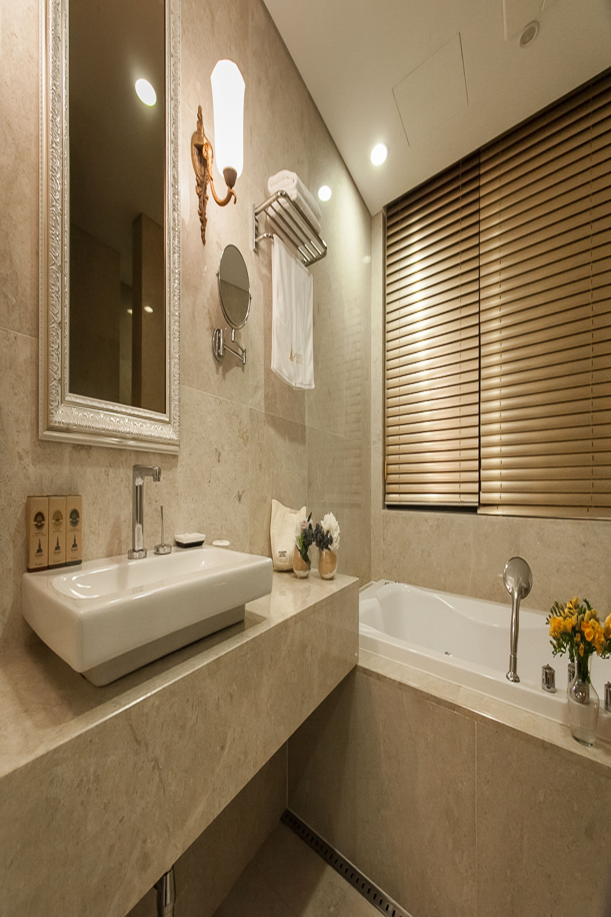 A modern bathroom with a large mirror, two sinks, a bathtub, and a window with blinds.