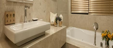 Un baño moderno con un espejo grande, dos lavamanos, una bañera y un ventanal con persianas.
