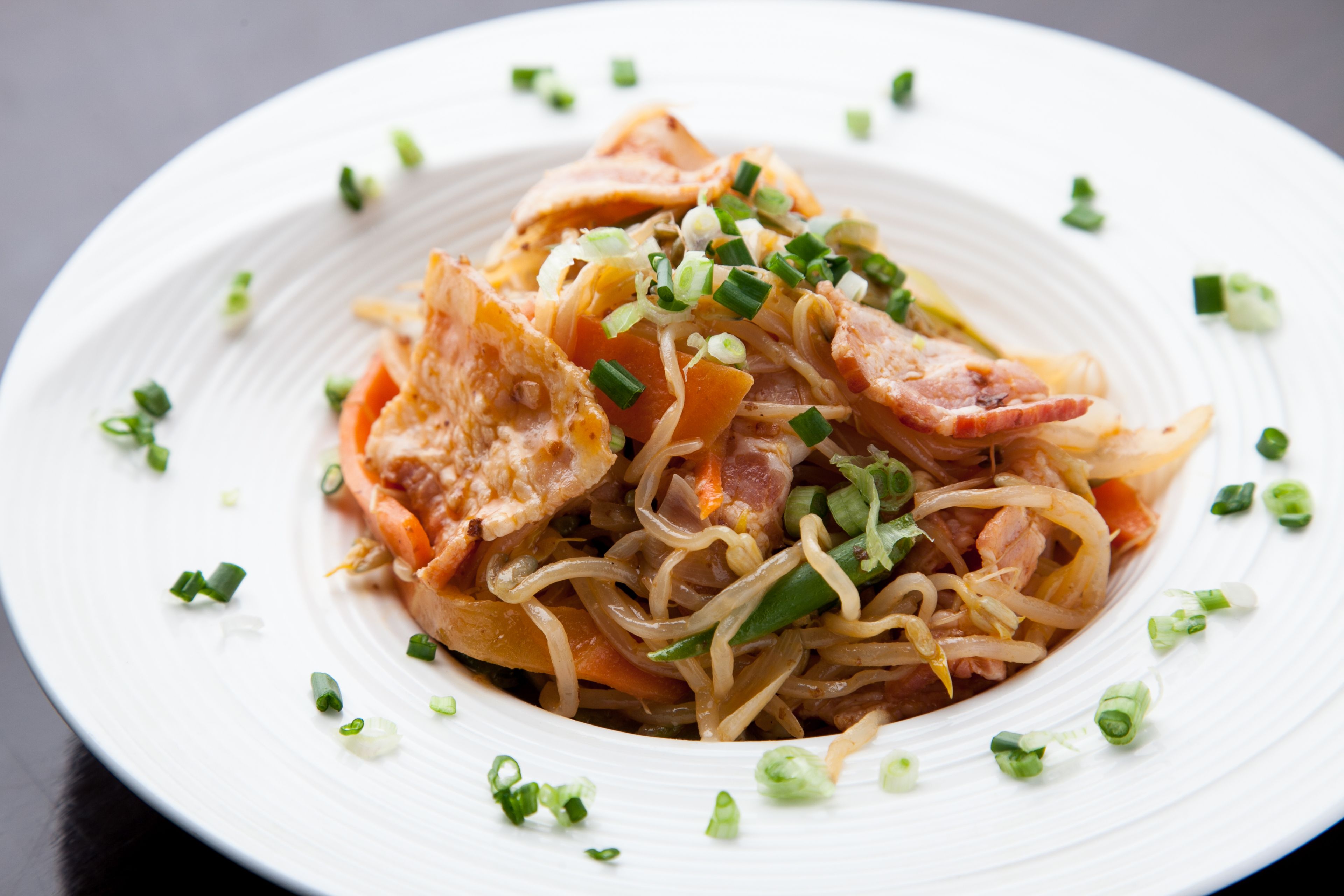A plate of noodles with vegetables and meat, garnished with chopped green onions.
