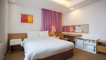 A hotel room with a bed, bedside table, desk, and a small refrigerator.