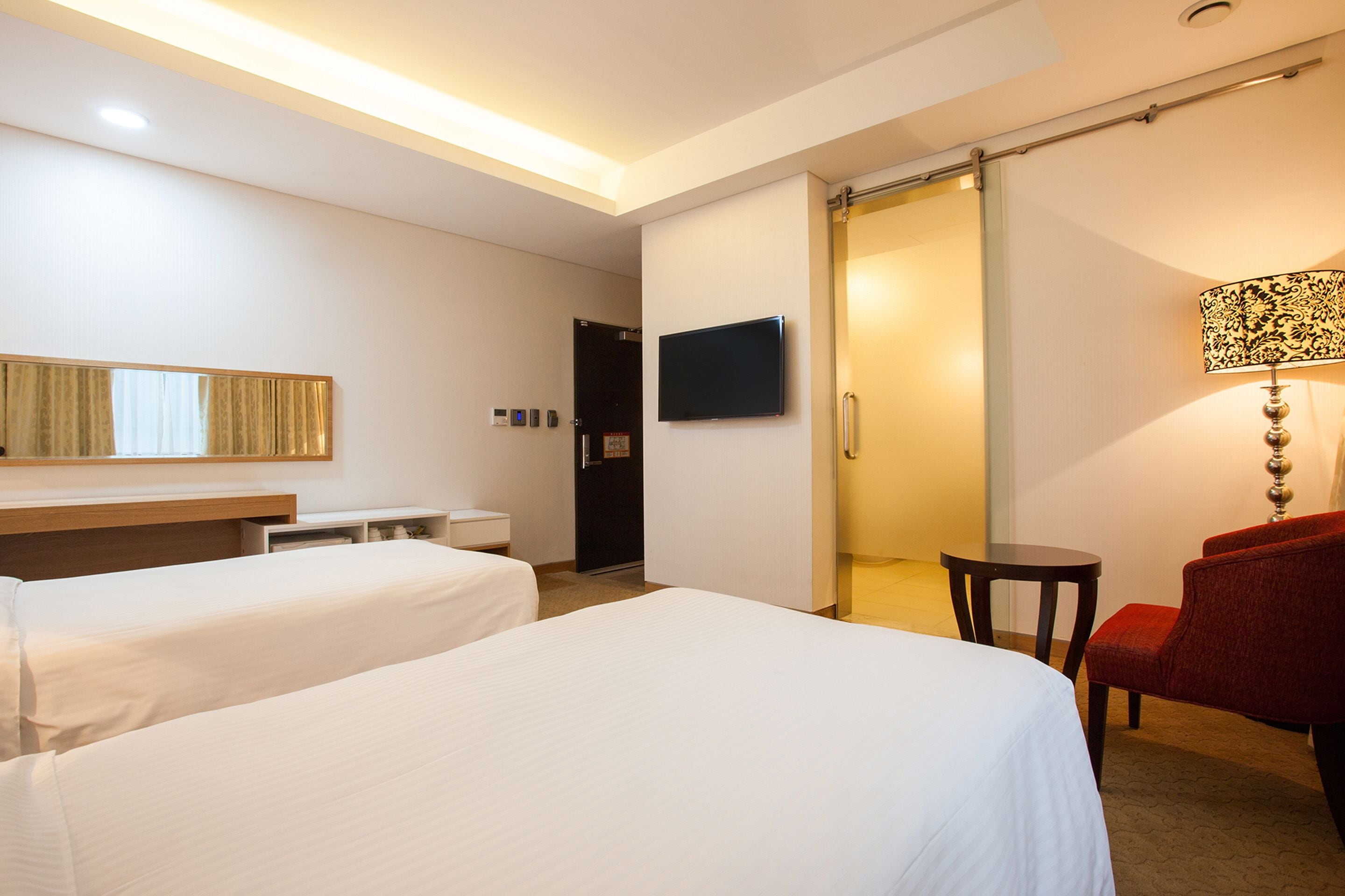 Habitación de hotel con dos camas, televisión, escritorio, silla y puerta corrediza.