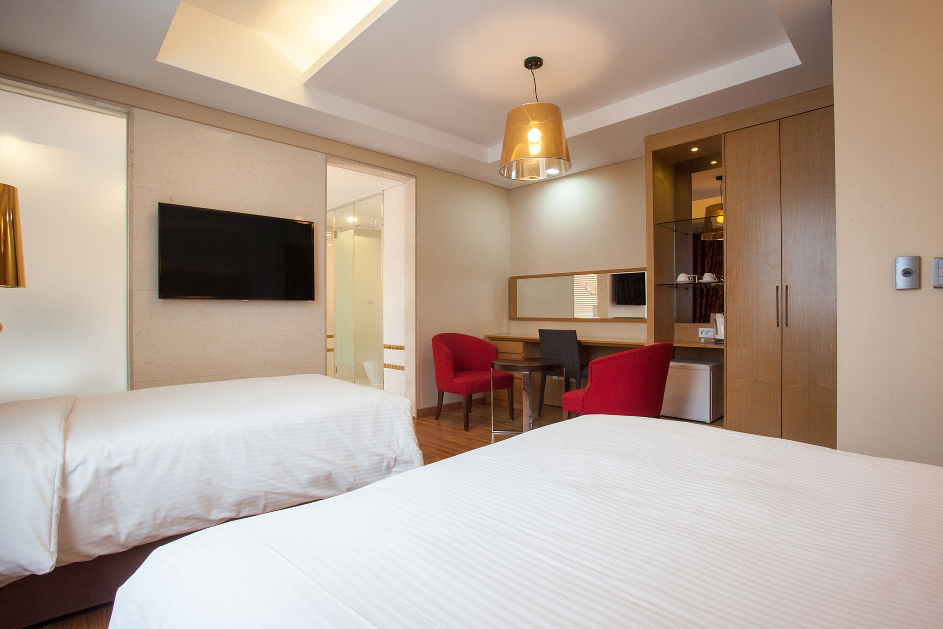 Une chambre d’hôtel avec deux lits, un bureau, une chaise, une télévision et une armoire.