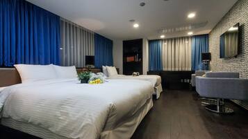 A modern hotel room with two beds, a sitting area, a vanity with a mirror, and a large window with curtains.
