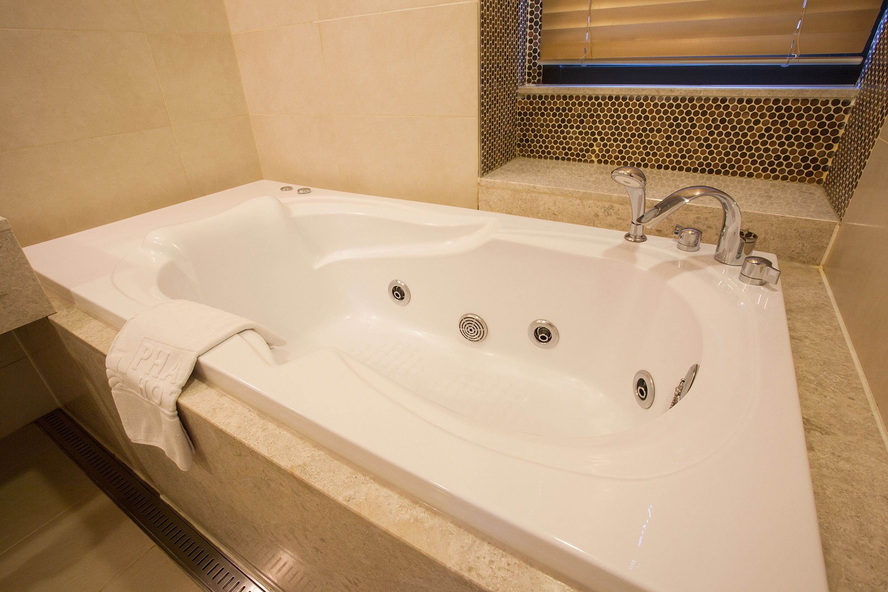 A white bathtub with a single faucet and two drains, a towel hanging on the side, and a tiled wall with a decorative pattern.