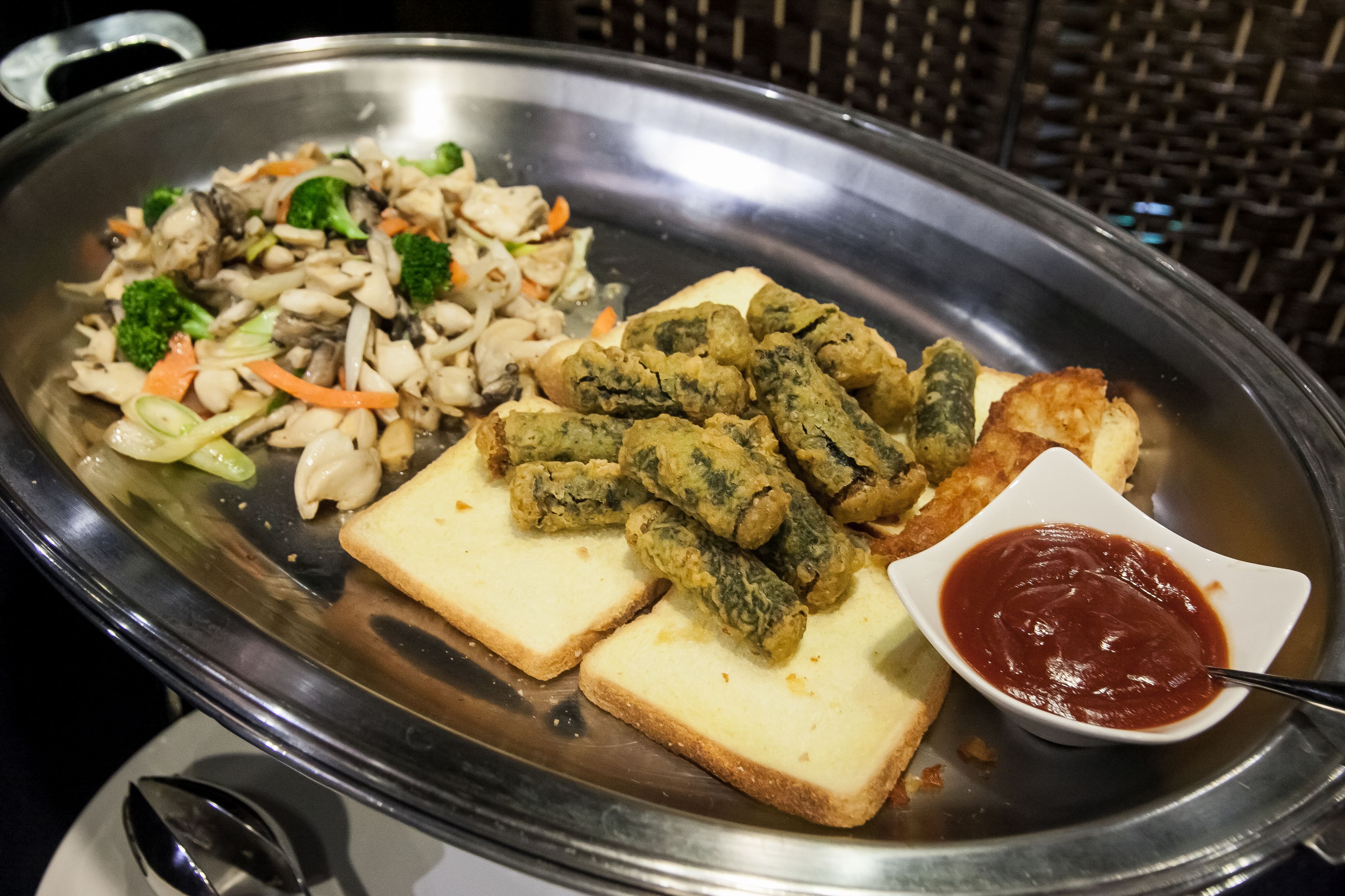 A stainless steel serving tray with fried items, sliced bread, and a small bowl of sauce.