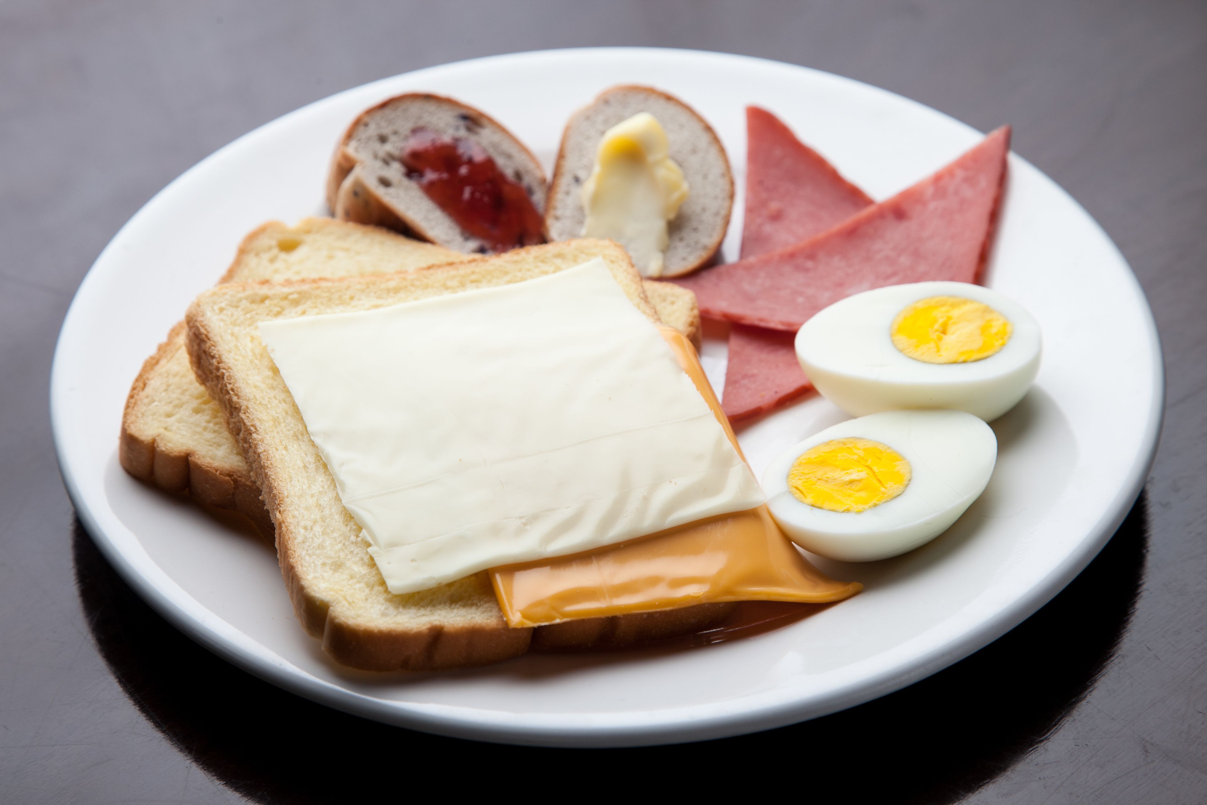 A plate with slices of bread, cheese, ham, and a boiled egg.