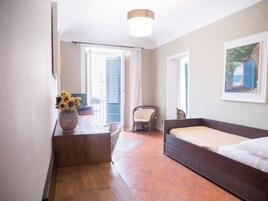 Un dormitorio con cama, una silla, una mesa con un jarrón de flores y un cuadro en la pared.