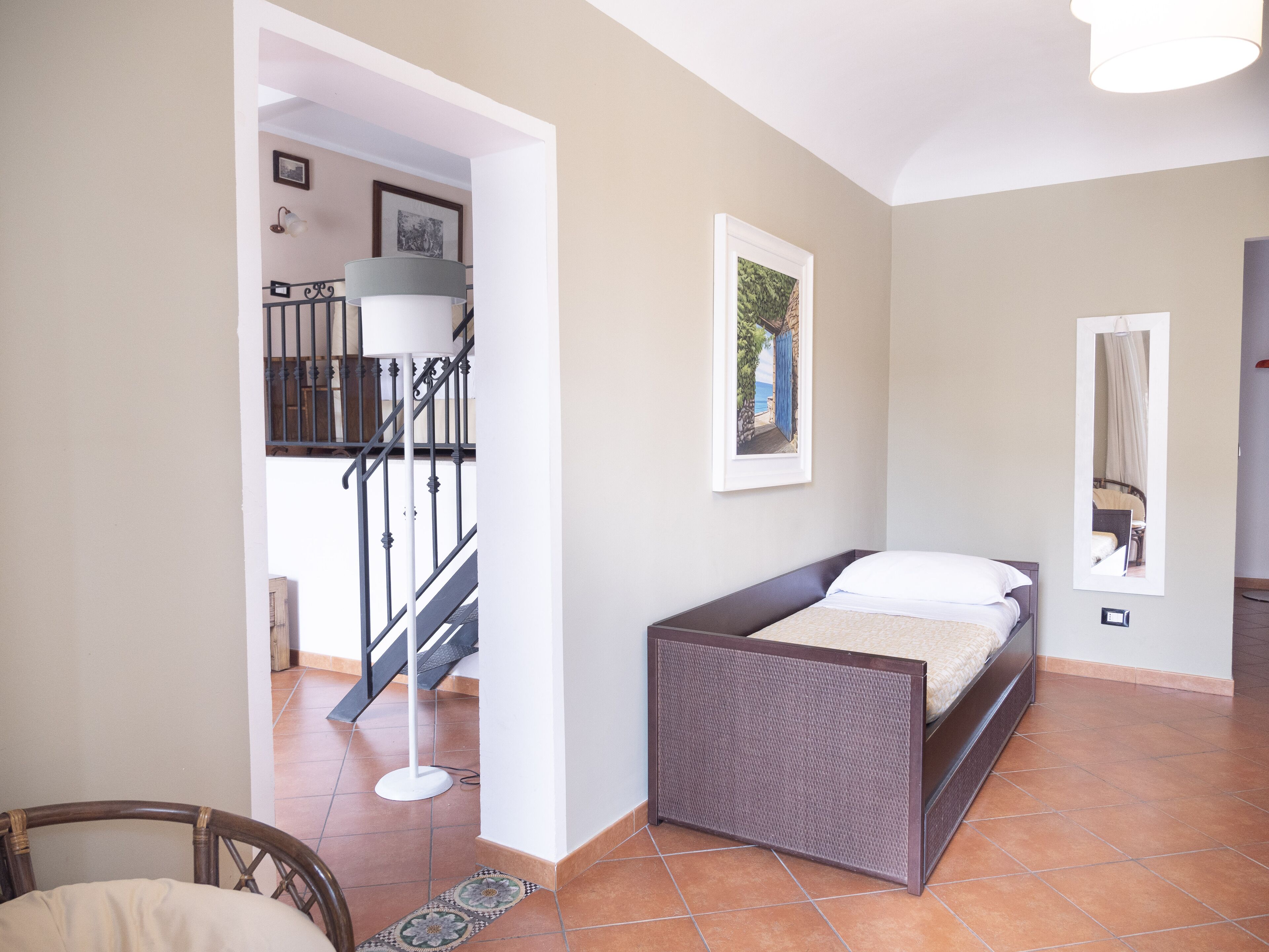 A bedroom with a bed, a small table, a chair, a lamp, and a staircase leading to an upper level.