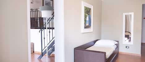 A bedroom with a bed, a small table, a chair, a lamp, and a staircase leading to an upper level.
