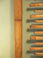 Une flûte en bambou, placée verticalement contre un mur vert.