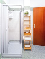 Un baño con cabina de ducha, un estante de madera con toallas y una puerta de madera.