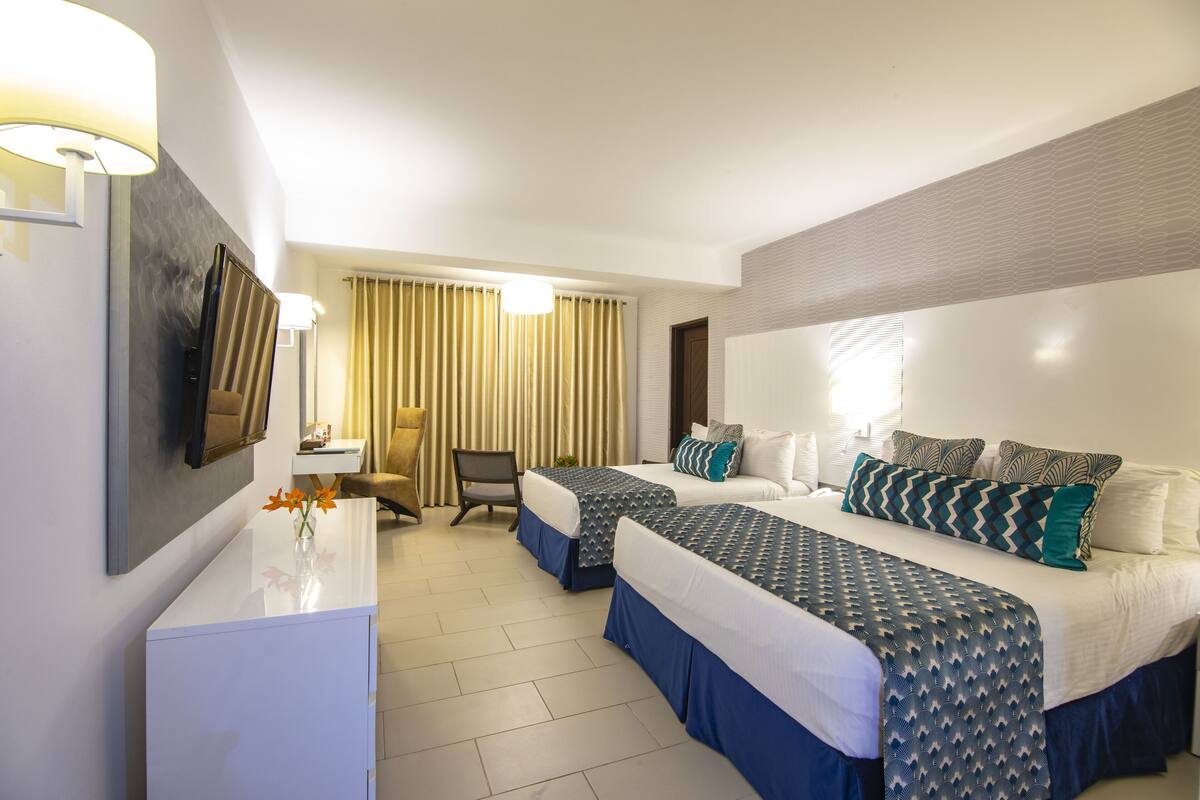 Habitación de hotel con dos camas, un escritorio, una silla y un televisor.