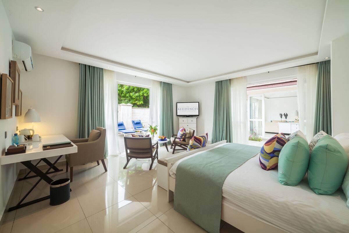 Habitación de hotel moderna con cama, escritorio y zona de estar. Hay un televisor en la pared y una ventana con cortinas.