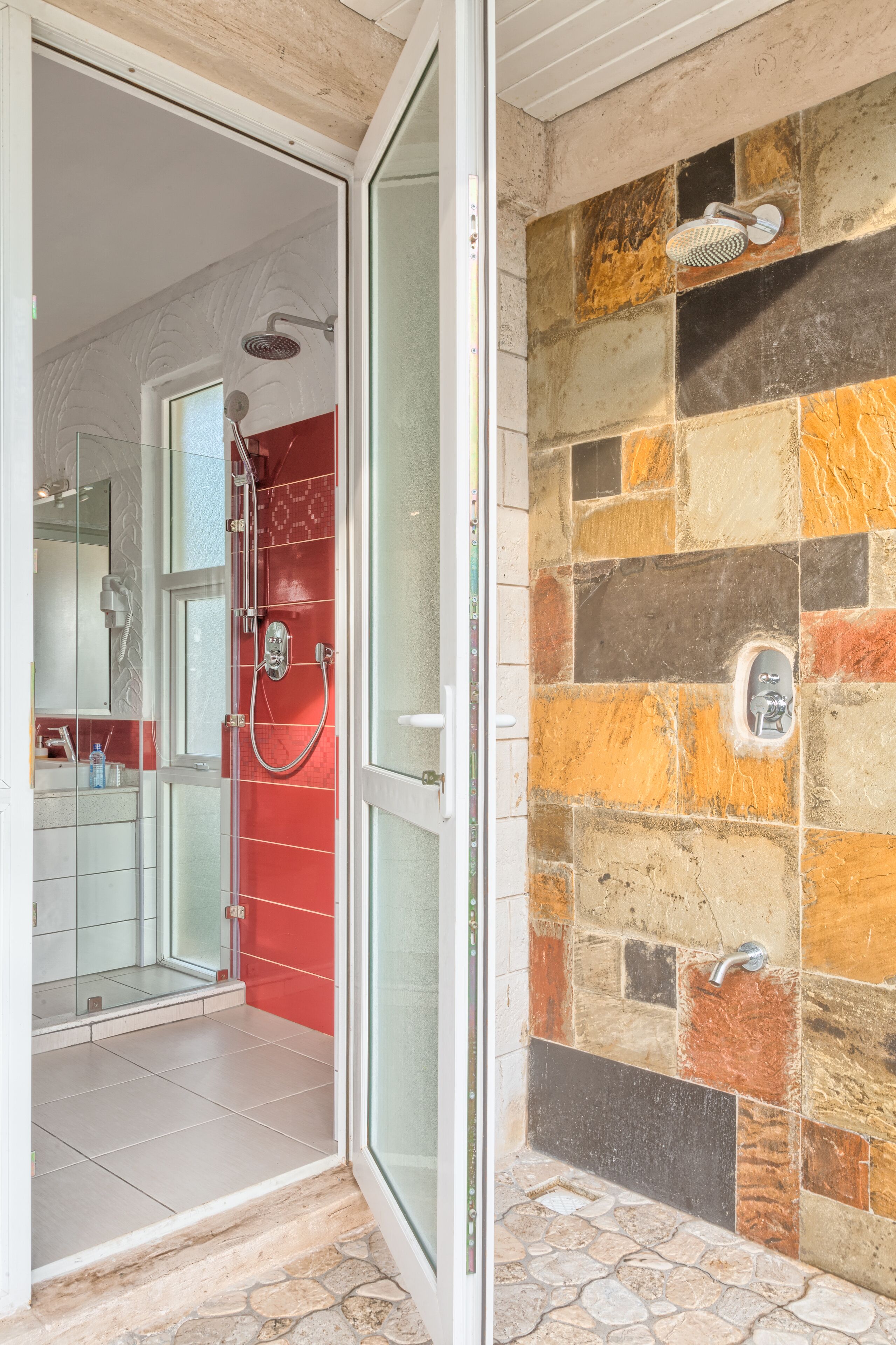 Ein modernes Badezimmer mit Duschabtrennung aus Glas, einer roten Akzentwand und einem Mosaikfliesen-Design.