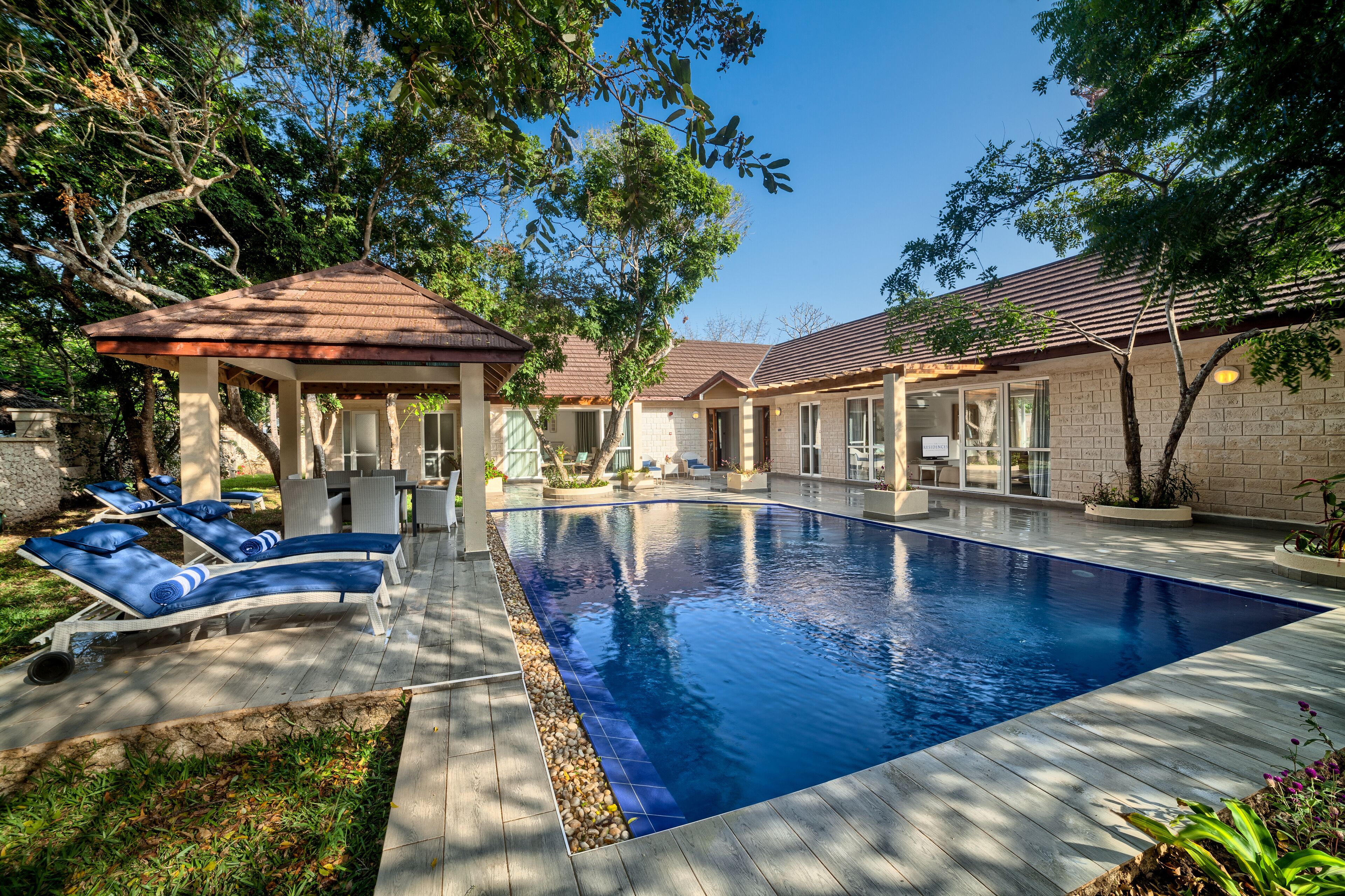 A swimming pool with lounge chairs, a gazebo, and a brick building with large windows.