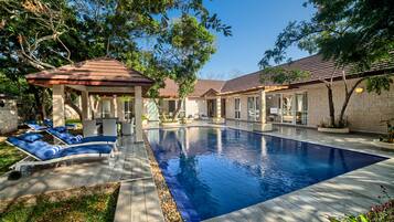 A swimming pool with lounge chairs, a gazebo, and a brick building with large windows.