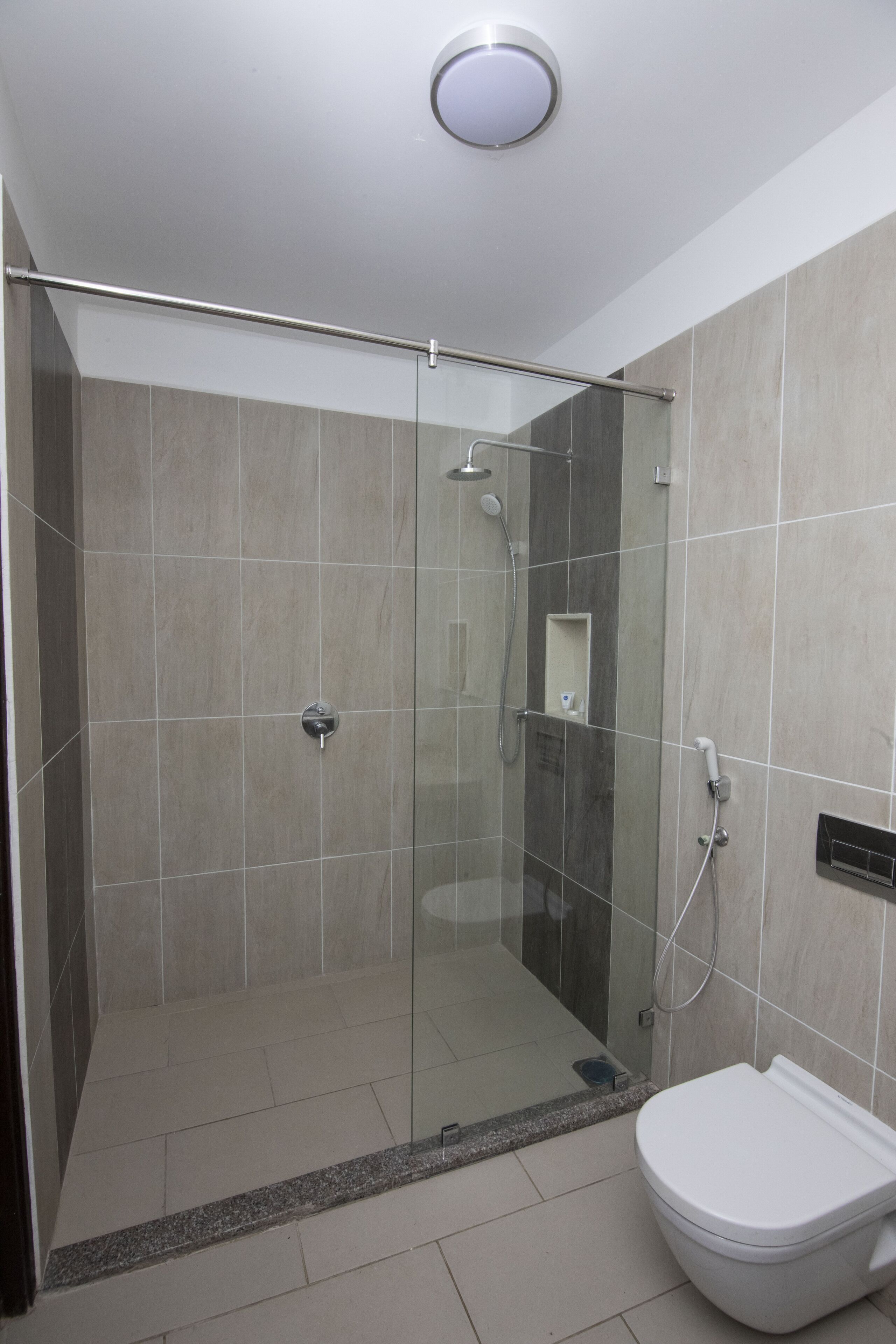 A modern bathroom with a glass-enclosed shower, a toilet, and tiled walls.