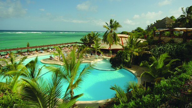 Ein Resort-Poolbereich mit mehreren Schwimmbecken, Palmen und Blick auf den Ozean.