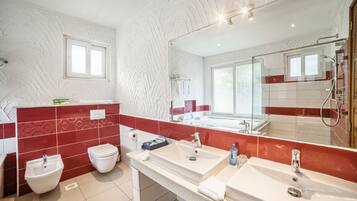 A modern bathroom with a large mirror, two sinks, a bidet, and a shower.