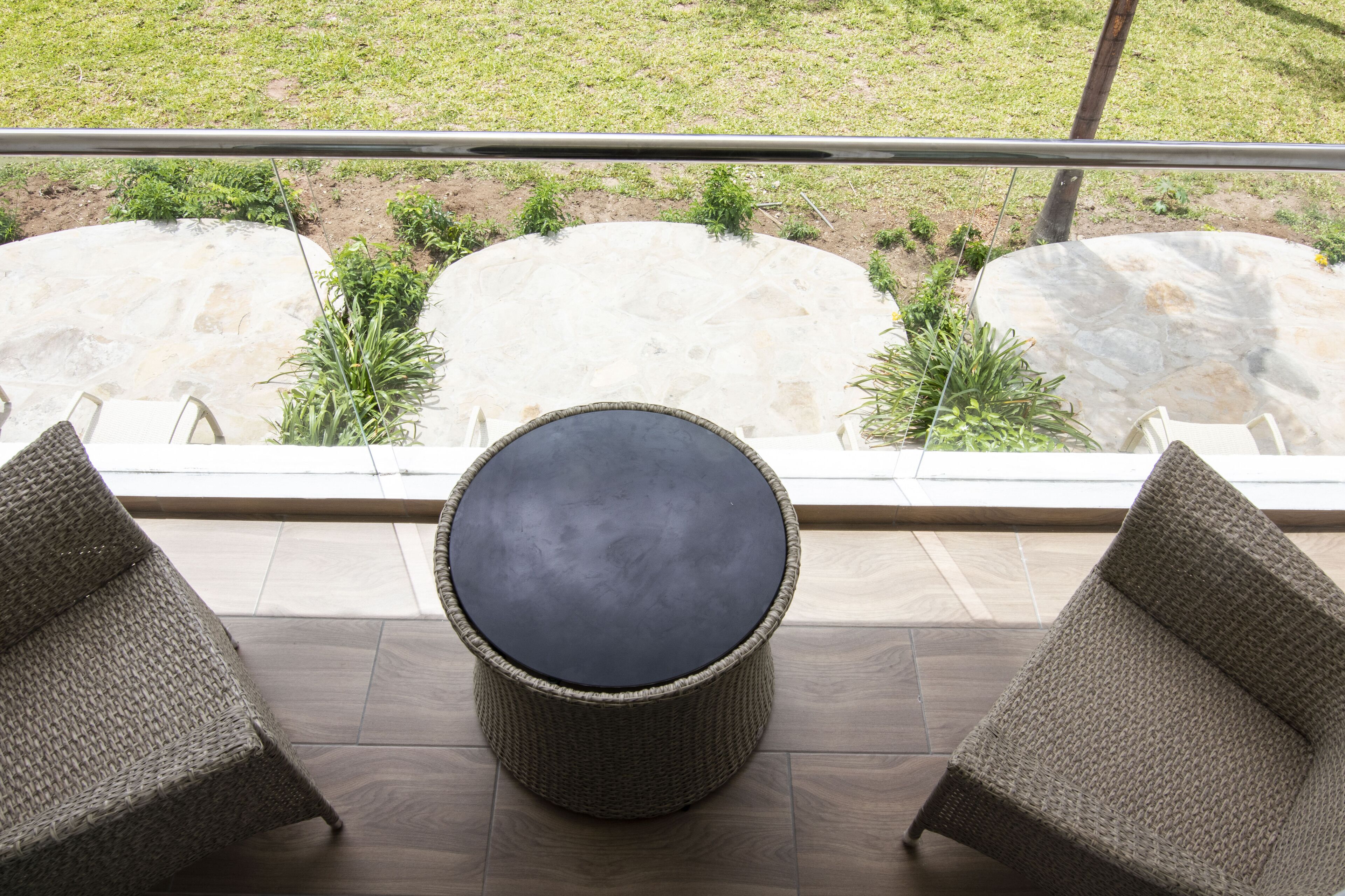 A balcony with wicker furniture, a round table, and a view of a landscaped garden.