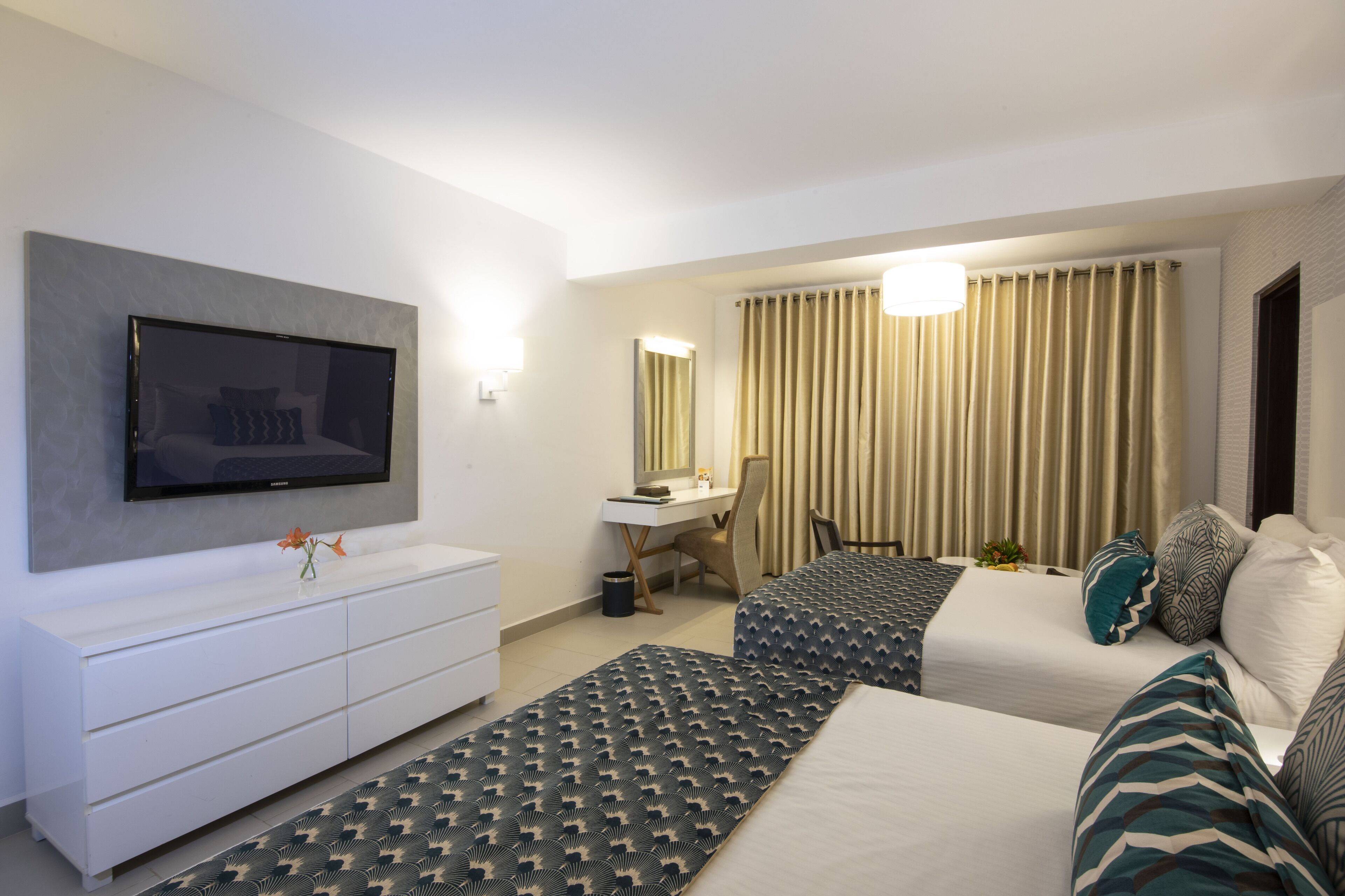 Ein Hotelzimmer mit einem Bett, einem Schreibtisch, einem Fernseher und einem großen Fenster mit Vorhängen.