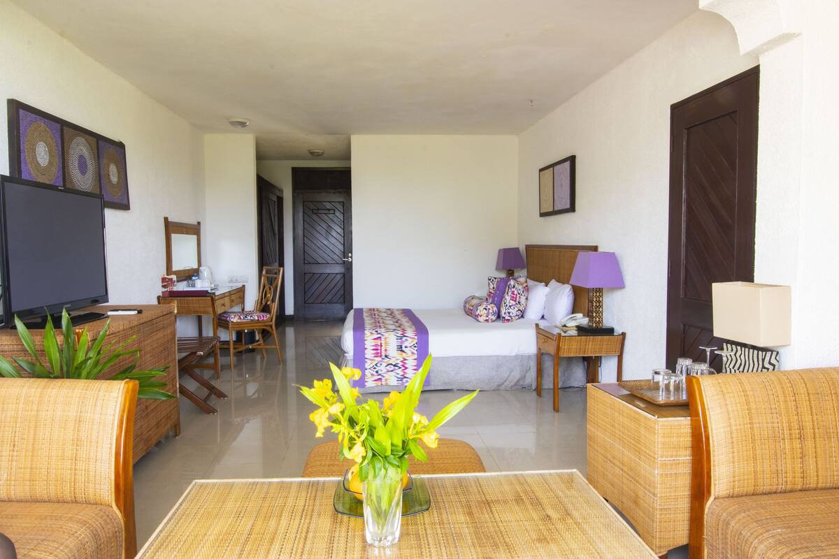 Habitación de hotel con cama, televisor, escritorio y zona de estar con mesa y sillas.