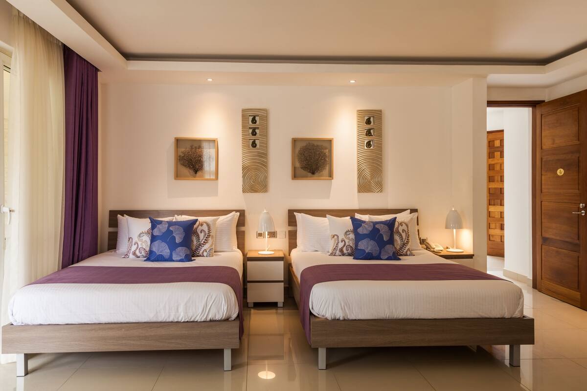 Habitación doble con dos camas, mesitas de noche, lámparas y cuadros en las paredes.