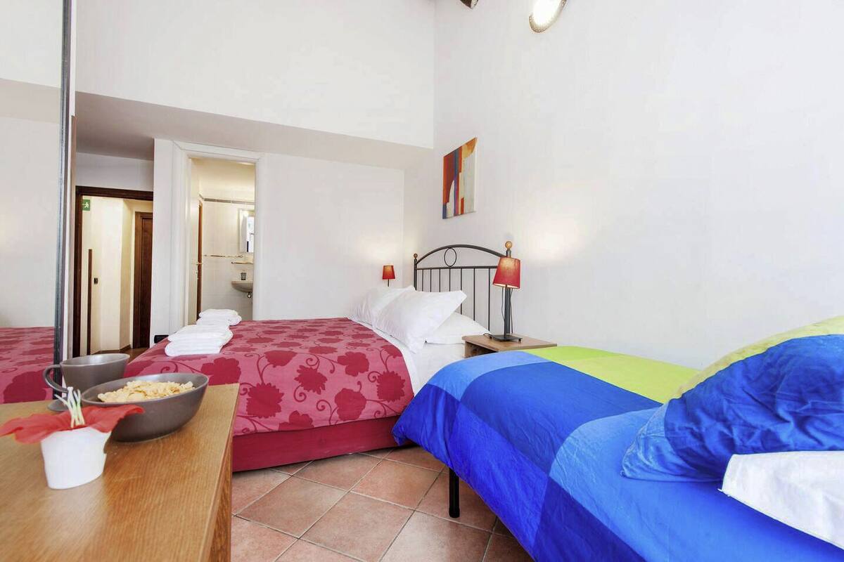 A hotel room with two beds, a wooden table with a bowl of fruit, and a mirror reflecting the room.
