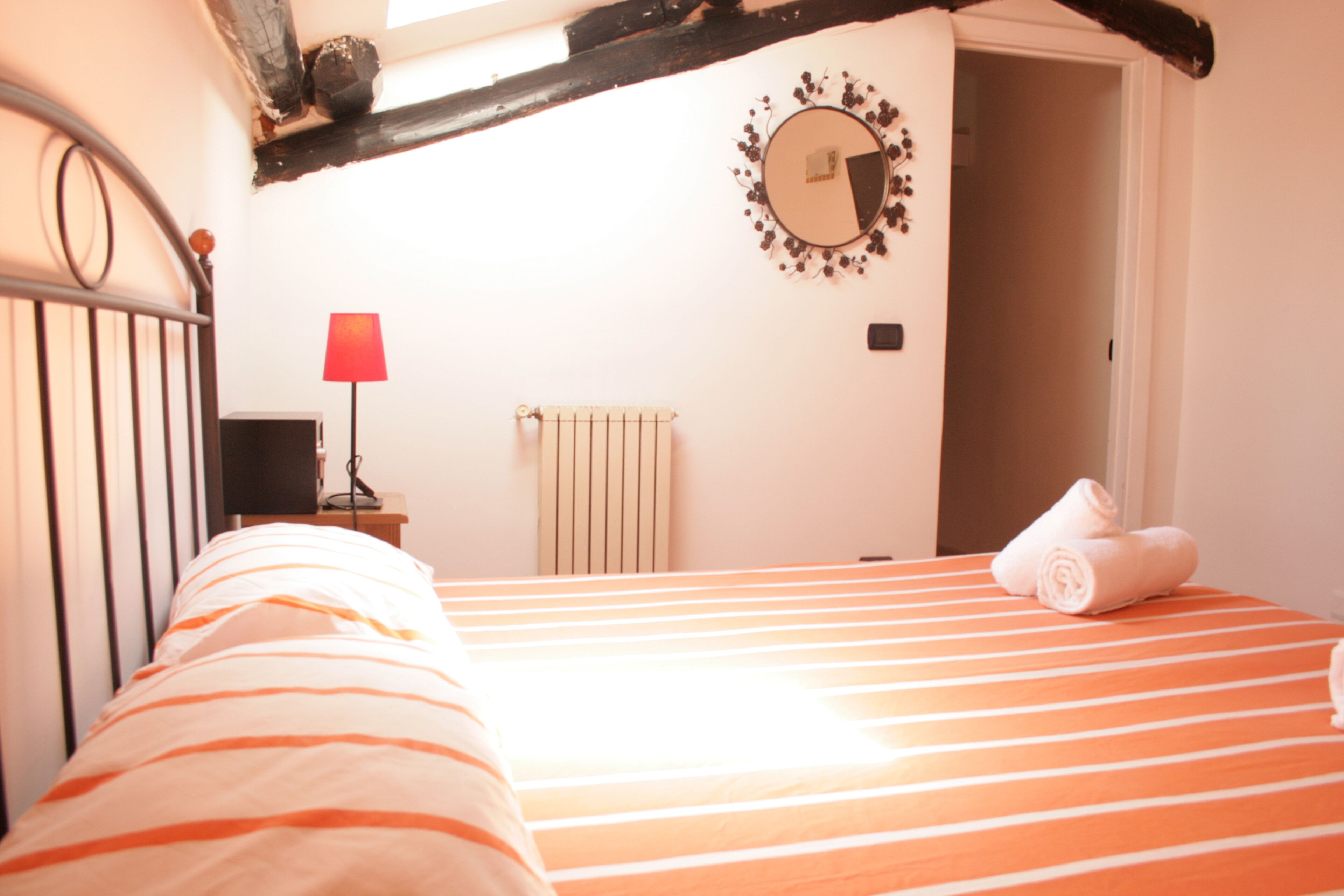A bedroom with a striped bed, a red lamp, a mirror, and a radiator.
