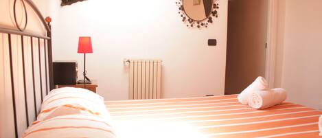 A bedroom with a striped bed, a red lamp, a mirror, and a radiator.