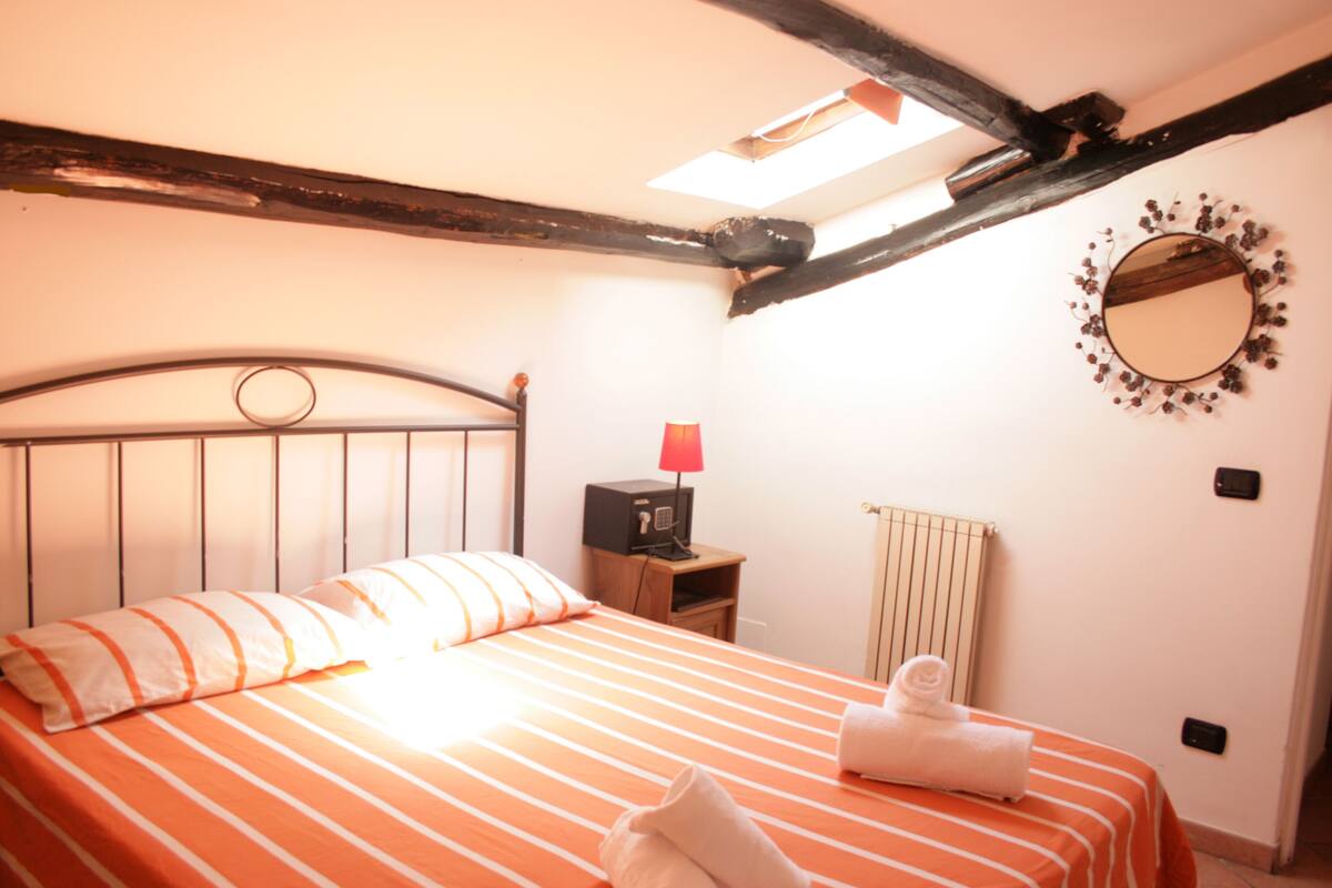 A bedroom with a bed, a nightstand, a lamp, a mirror, and a radiator.