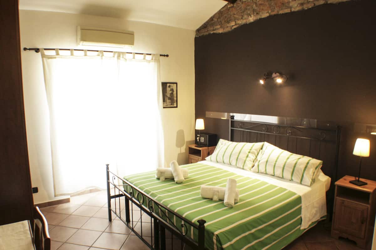 A hotel room with a bed, two bedside lamps, a nightstand, a picture on the wall, and a window with curtains.