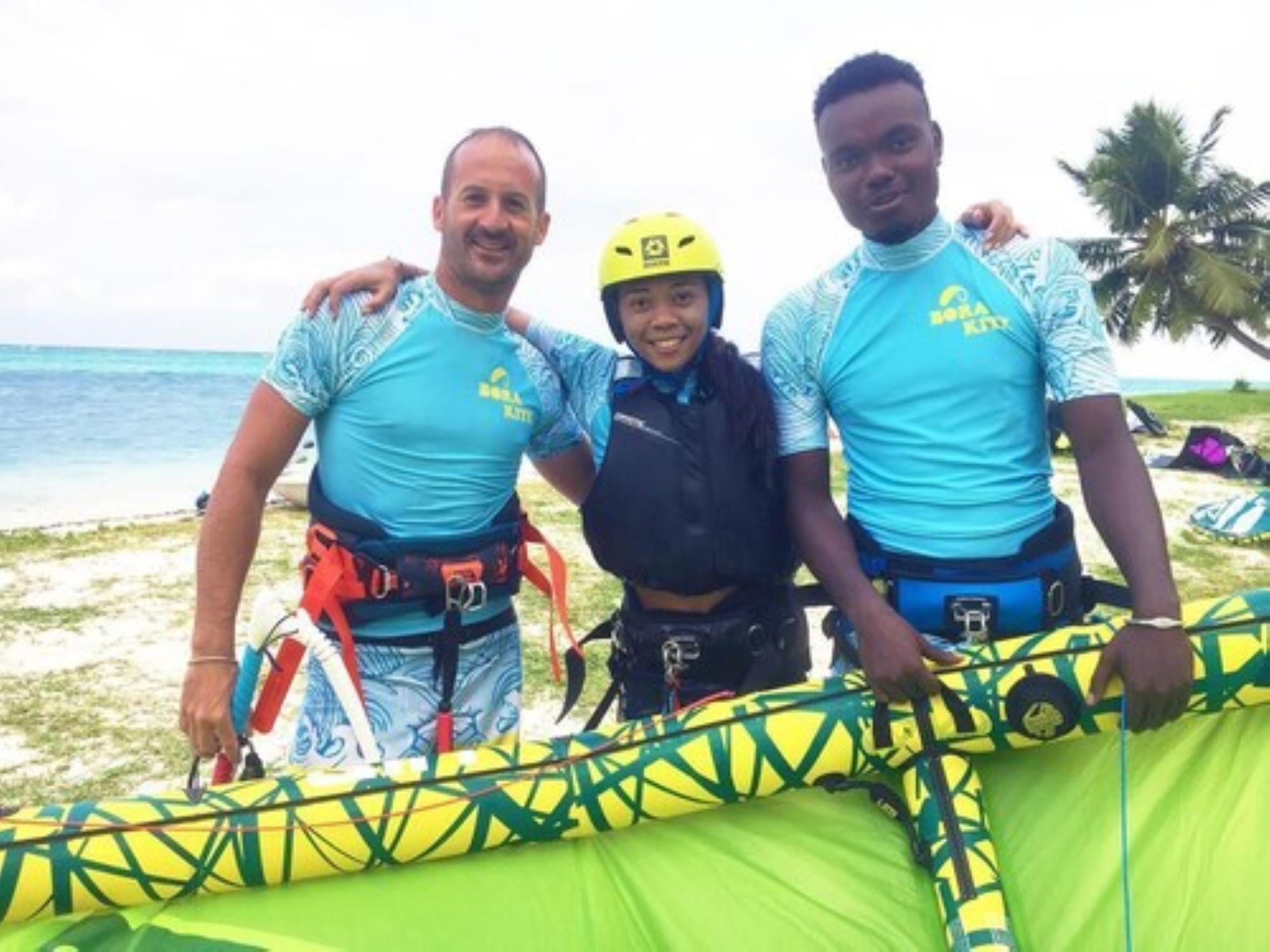 Three people standing by a green inflatable raft on a beach.