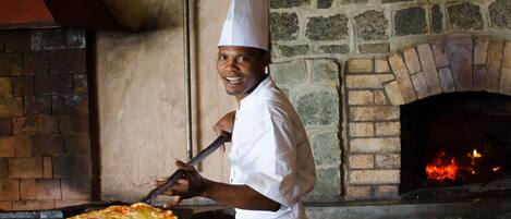 Un chef con uniforme y gorro blanco usa un utensilio de mango largo para introducir una pizza en un horno de ladrillo.