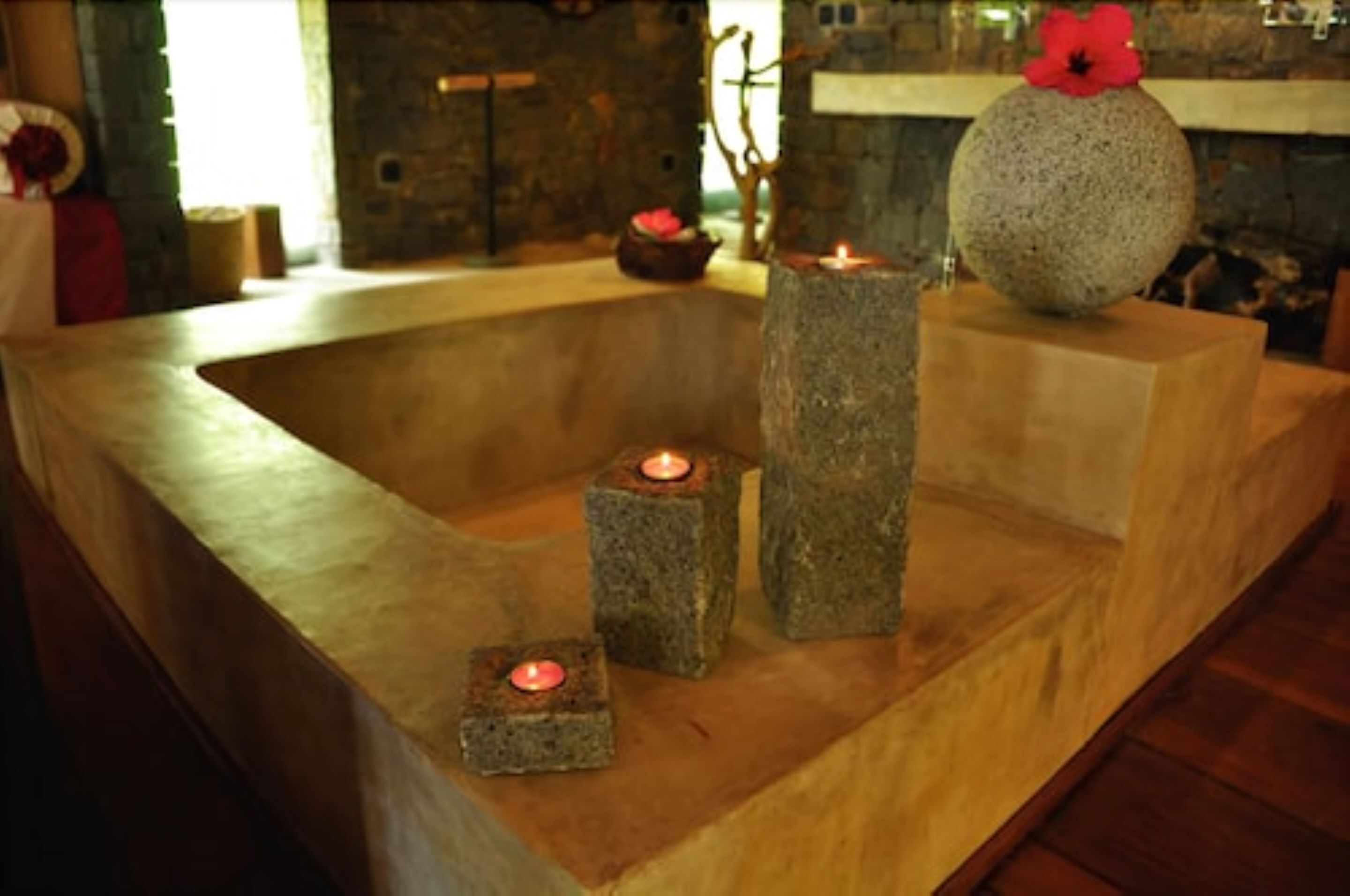 Une baignoire en pierre, décorée de bougies et d'une fleur.