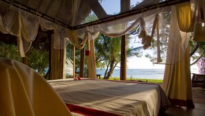 Una cama con detalles en rojo, vista al mar y una palmera.