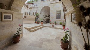 A courtyard with stone steps leading to a building entrance, surrounded by potted plants and framed pictures on the walls. - Magic Cave House (Ürgüp)