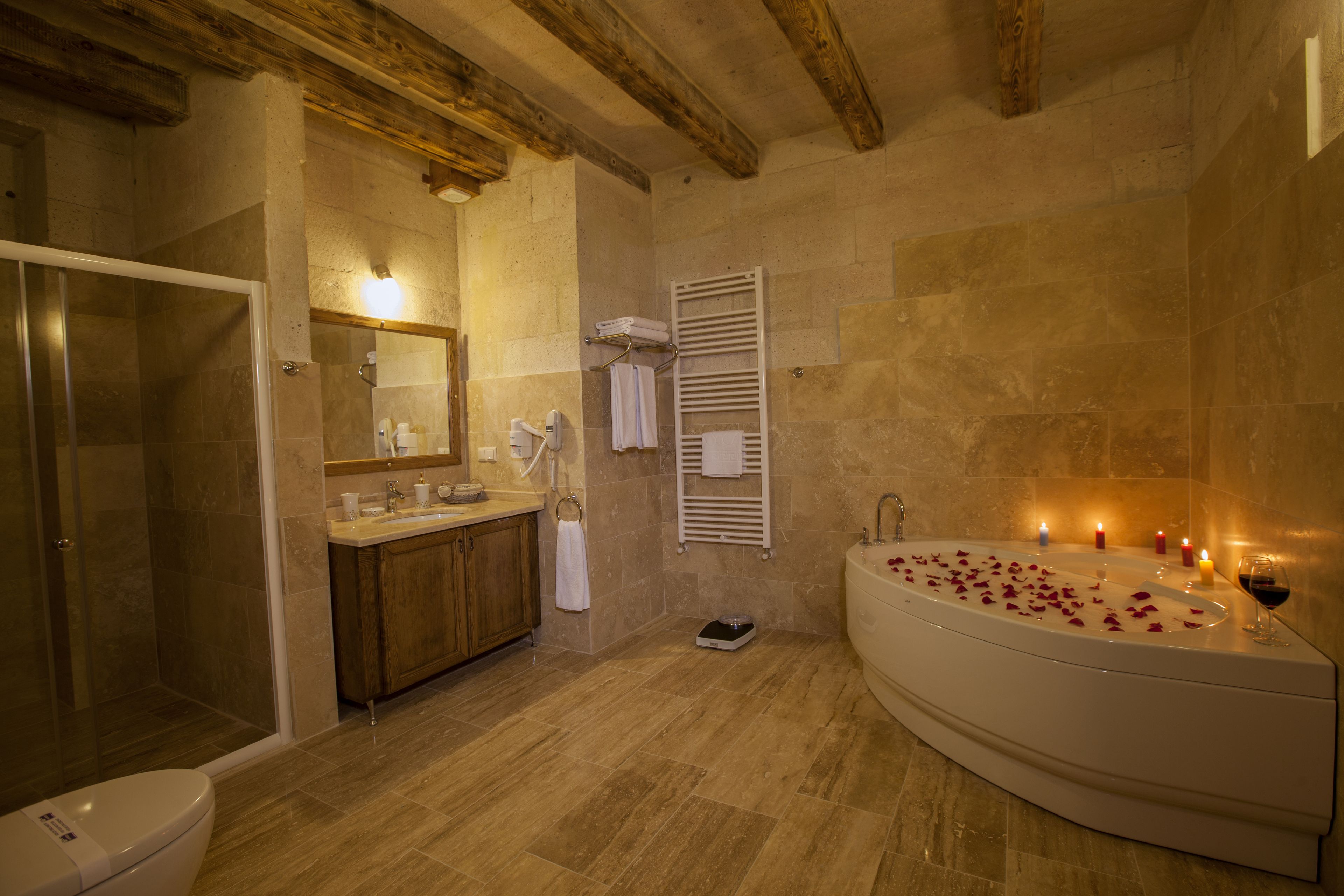 A bathroom with a shower, toilet, sink, and a large bathtub with candles and rose petals.