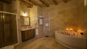 A bathroom with a shower, toilet, sink, and a large bathtub with candles and rose petals.
