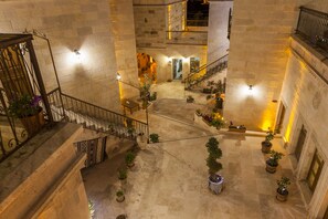 Un atrio de varios niveles con paredes de piedra, una escalera central y plantas en macetas.