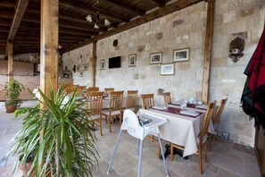 Un área de comedor al aire libre con paredes de piedra, vigas de madera y mesas preparadas para una comida.