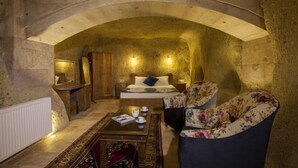 A cozy room with a stone archway, a bed with floral upholstery, a wooden nightstand, and a coffee table with a magazine. - Magic Cave House (Ürgüp)