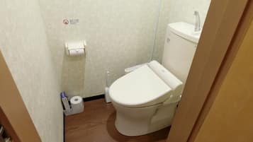 A small, compact bathroom with a toilet, a toilet paper holder, and a trash bin.