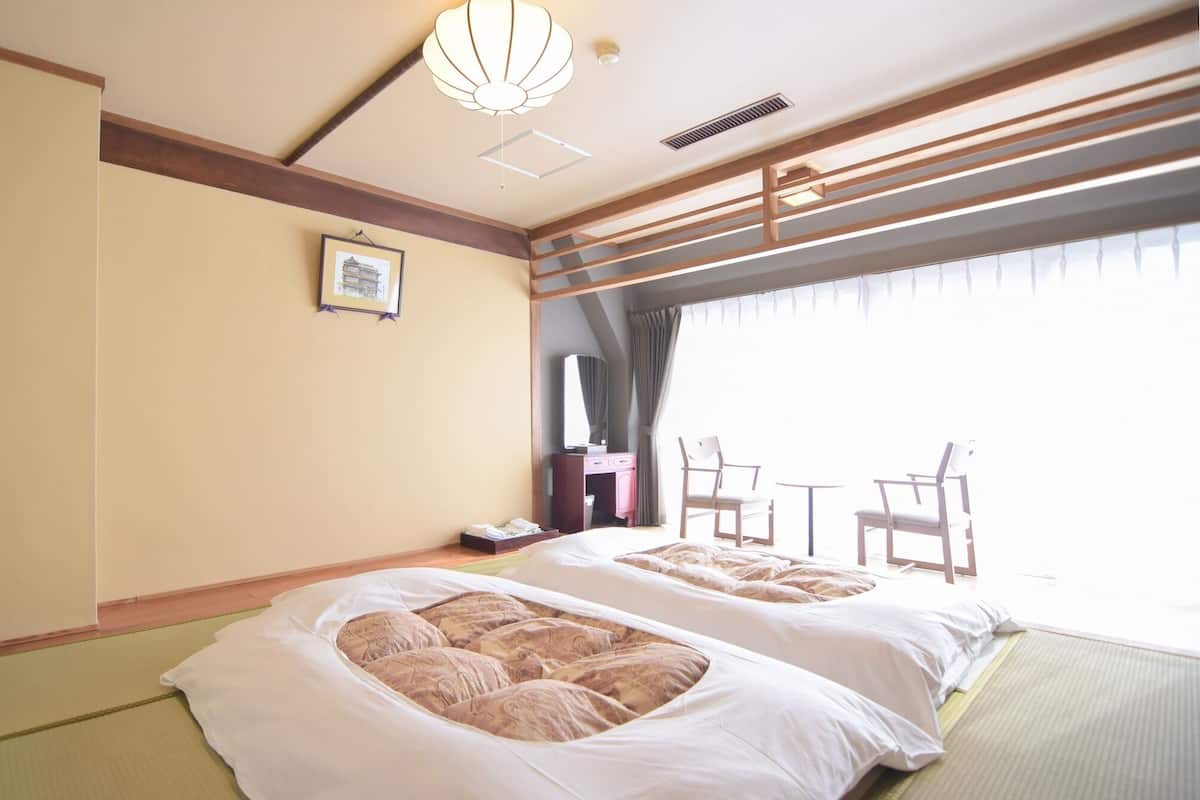 Ein Hotelzimmer mit zwei Betten, einem Schreibtisch, einem Stuhl und einem großen Fenster.