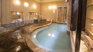 Un área de baño de aguas termales con paredes de azulejos, múltiples grifos y una piscina curva.
